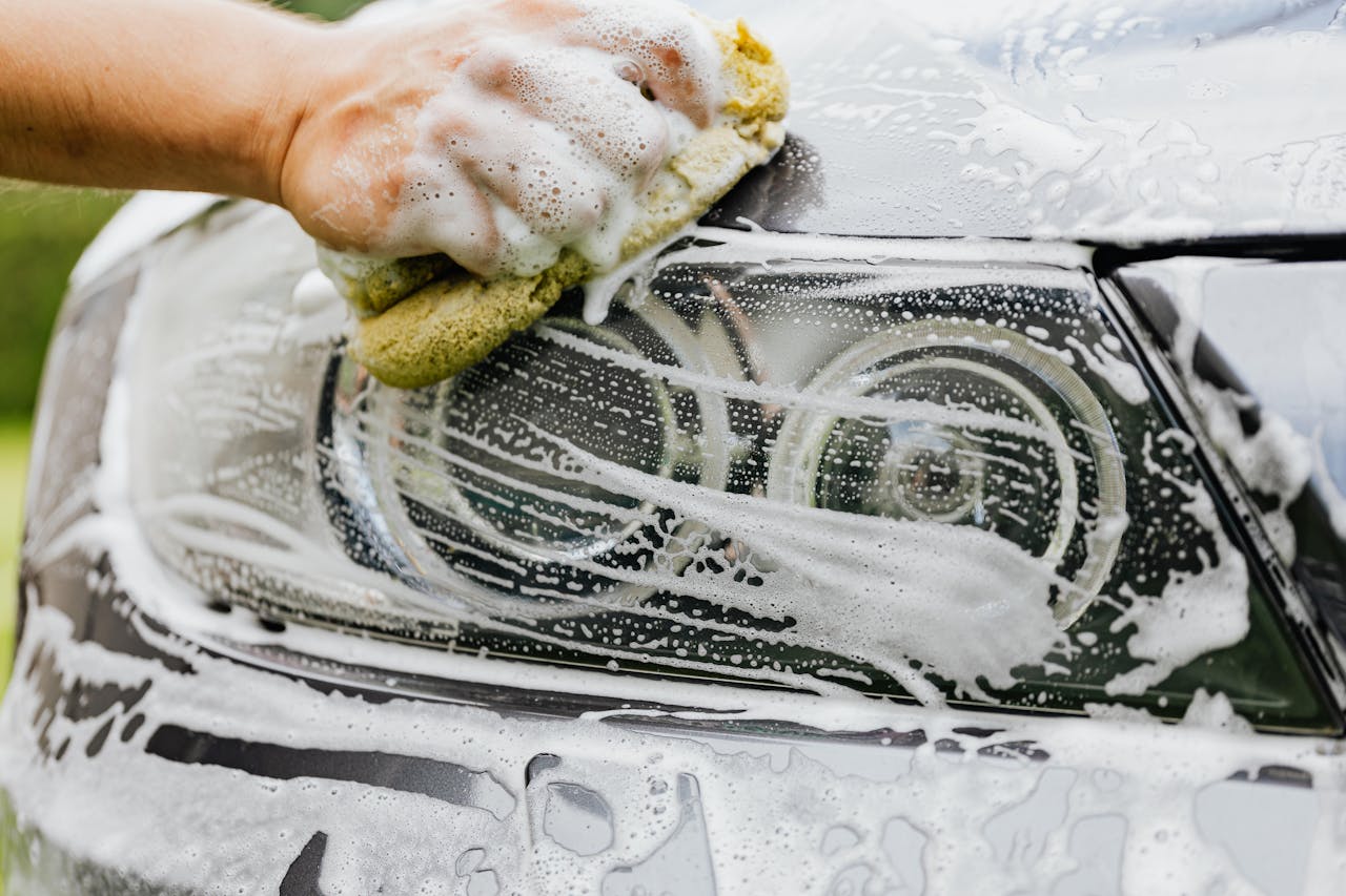 Mastering the First Impression: Your intriguing post title goes here Hand scrubbing a car headlight with sponge and soap suds, detailing process.